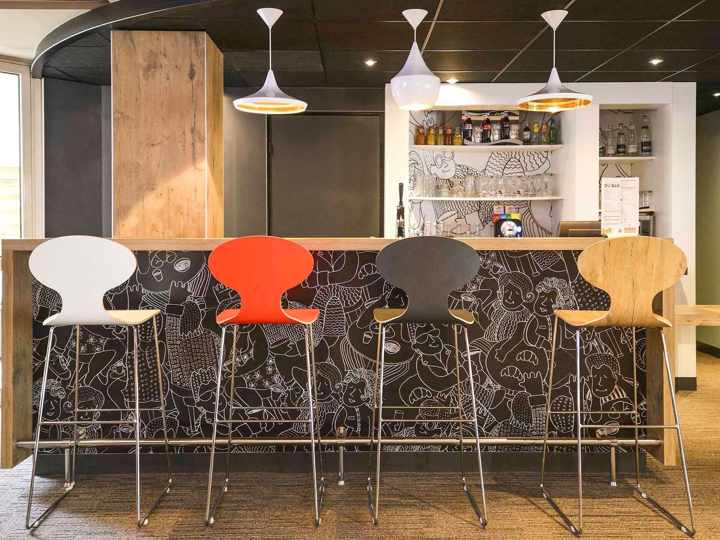 A bar area with a black and white patterned wall, a wooden counter, and five stools with different colors.