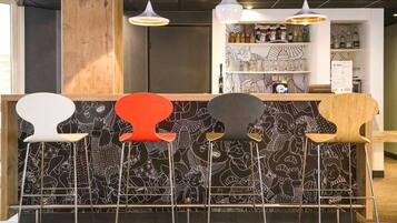 A bar area with a black and white patterned wall, a wooden counter, and five stools with different colors.