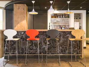 A bar area with a black and white patterned wall, a wooden counter, and five stools with different colors.
