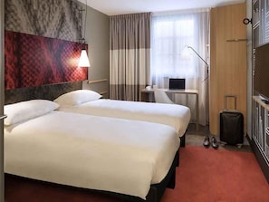 A hotel room with two beds, a desk with a laptop, a suitcase, and a wardrobe. - ibis Château de Fontainebleau (Fontainebleau)