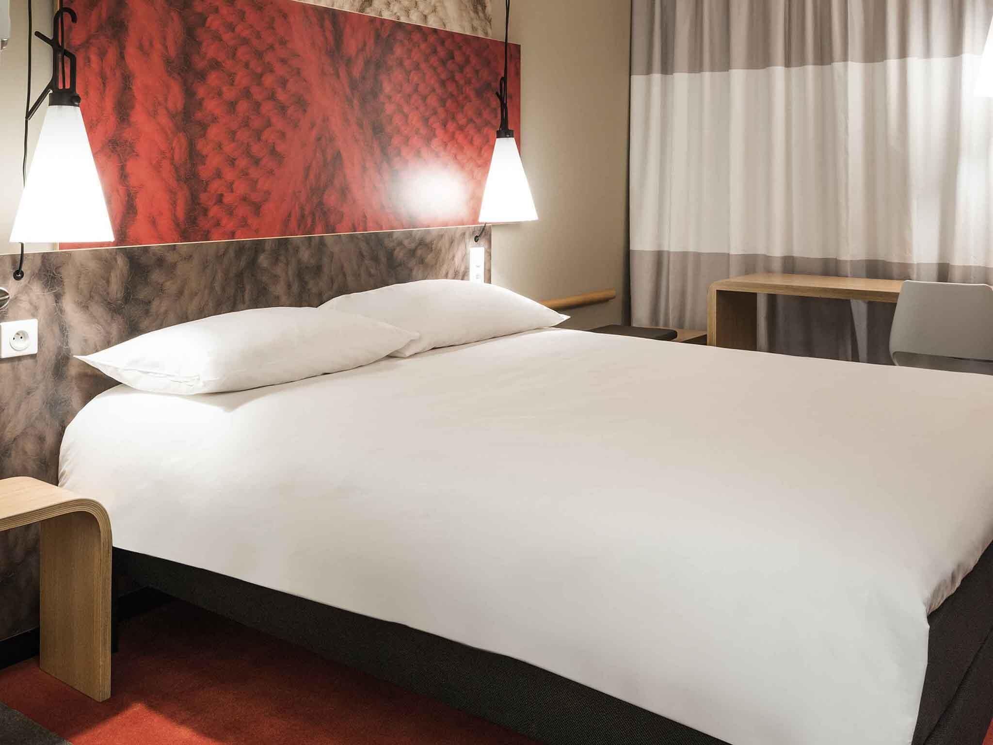 Une chambre d’hôtel avec un lit, deux lampes de chevet, une table de nuit en bois, une petite table et une chaise.