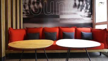 Un sofá rojo con cojines negros y rojos, dos mesas redondas y una pared con la palabra 'lounge' parcialmente visible.