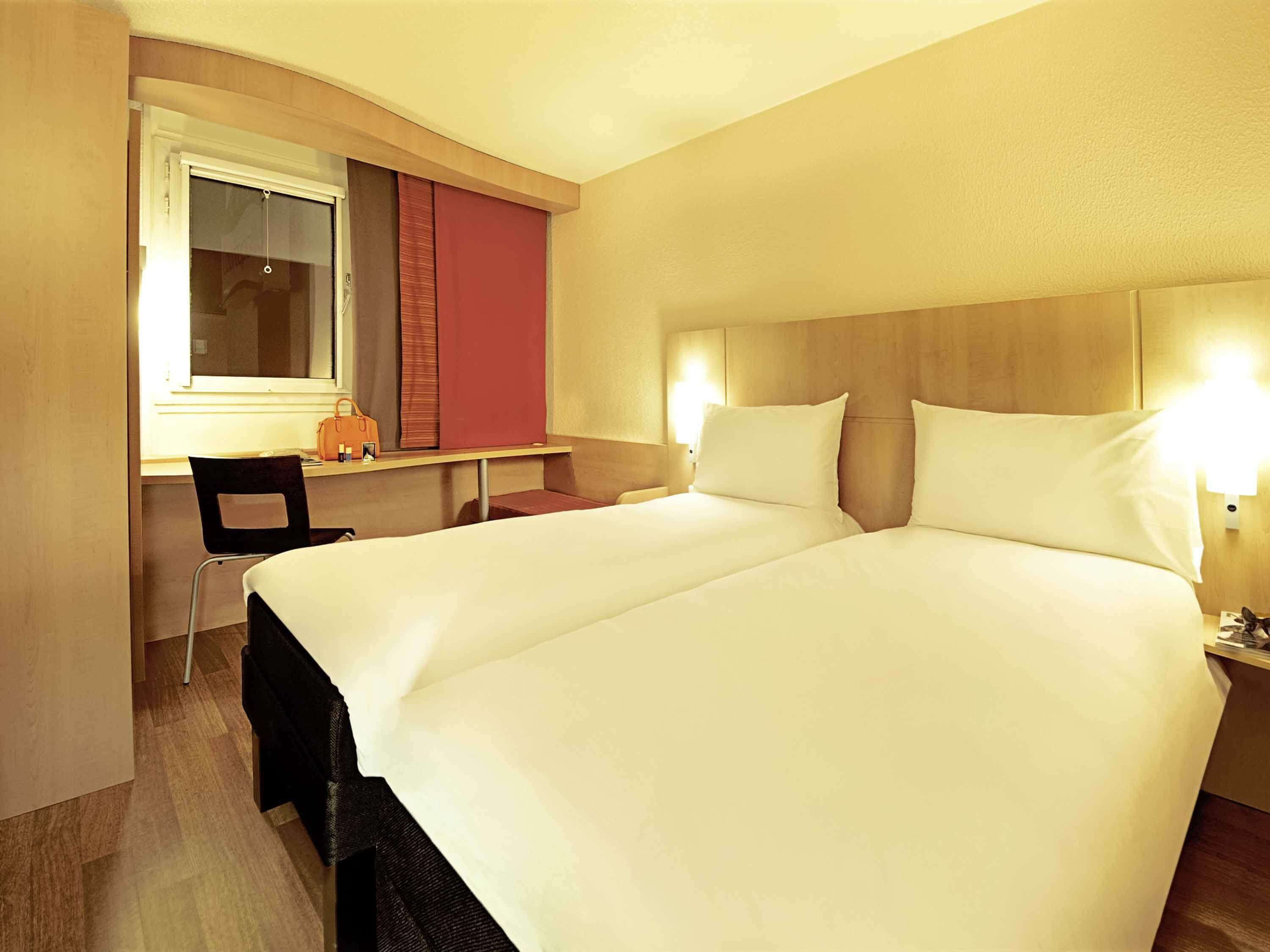 Habitación de hotel con una cama grande, un escritorio con silla y una ventana con cortinas.