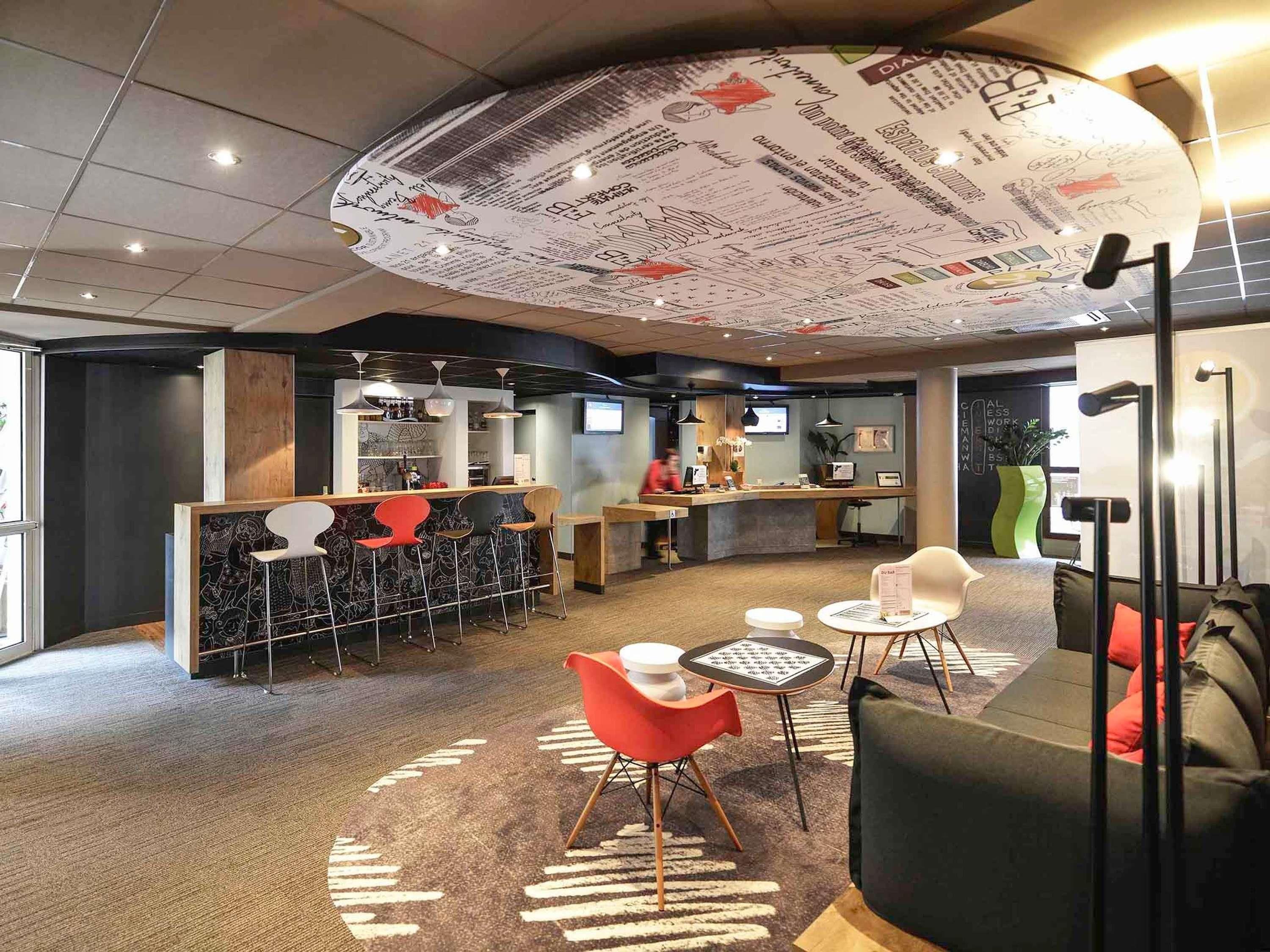 Un interior moderno con mostrador de recepción, zona de bar, asientos y un diseño de techo original.