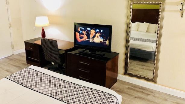 A hotel room with a TV on a desk, a bed with a checkered bedspread, a large mirror, and a lamp. - Budget Lodge (Chesapeake)