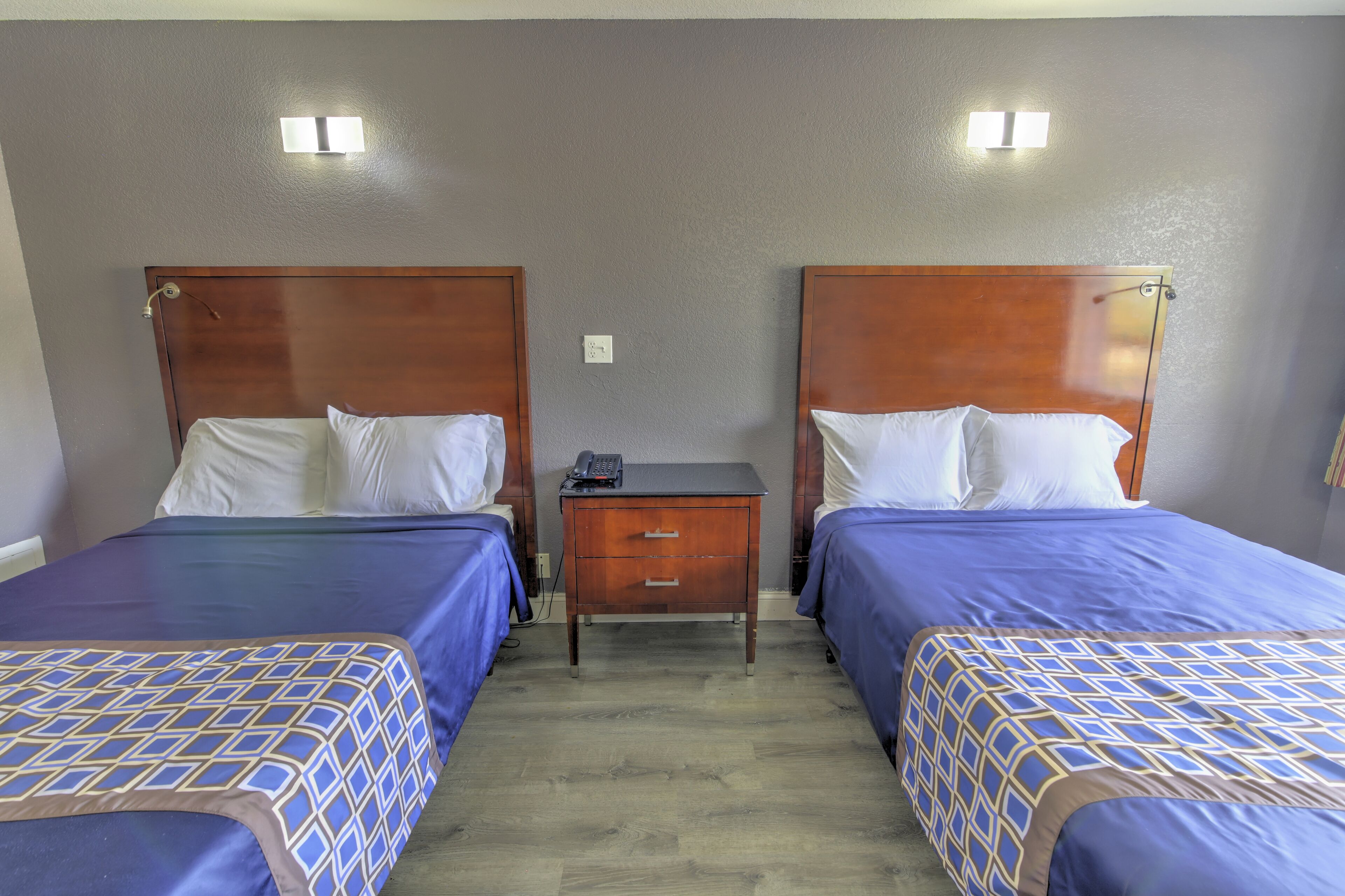 Habitación de hotel con dos camas, cada una con cabecero de madera, una mesita de noche de madera y una lámpara de pared.