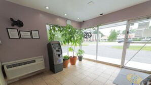 A reception area with a self-service kiosk, potted plants, and a view of the street outside. - Budget Lodge (Chesapeake)