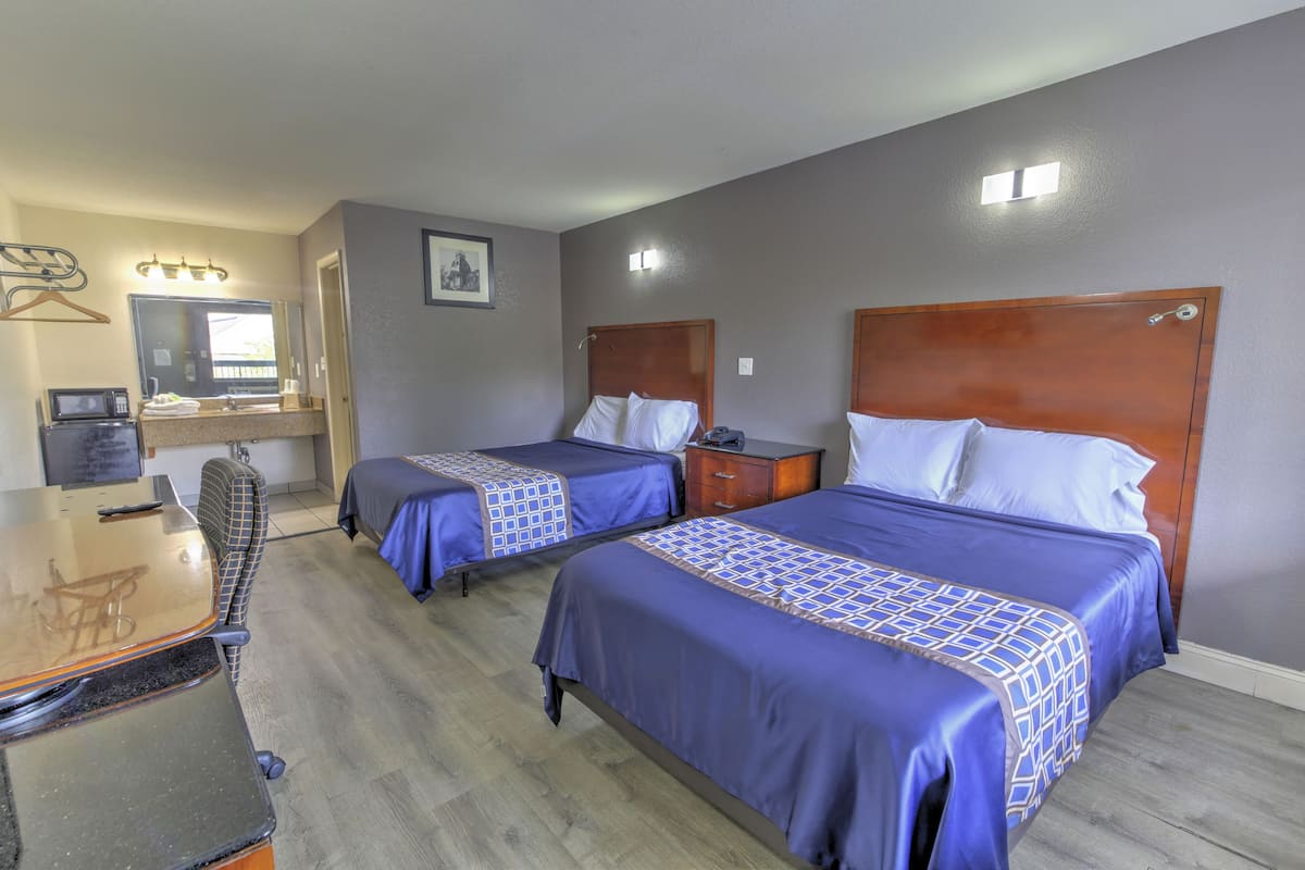 A hotel room with two beds, a desk, a chair, a mirror, and a small bathroom area.