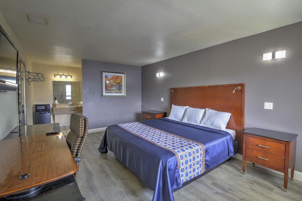 A bedroom with a bed, bedside tables, a dresser, a mirror, and a bathroom visible in the background.