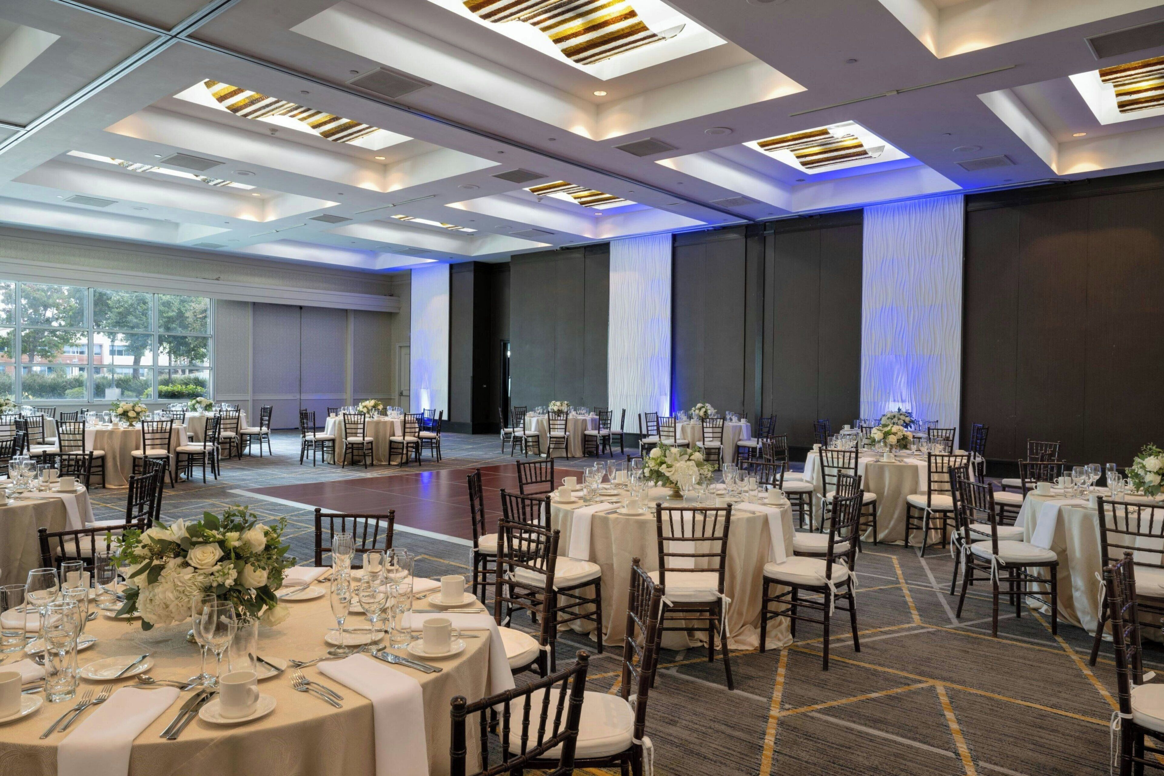 Un salón de banquetes con mesas redondas dispuestas para comer, con manteles blancos y centros de mesa florales.