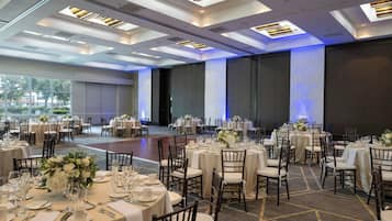 Un salón de banquetes con mesas redondas dispuestas para comer, con manteles blancos y centros de mesa florales.