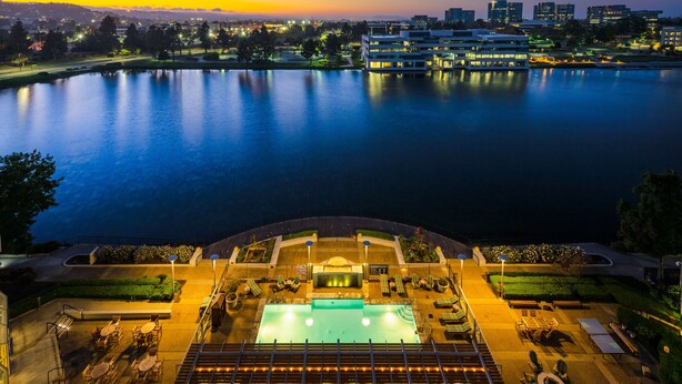 A hotel with a pool, outdoor seating, and a view of a city skyline at dusk. - Grand Bay Hotel San Francisco (Redwood City)