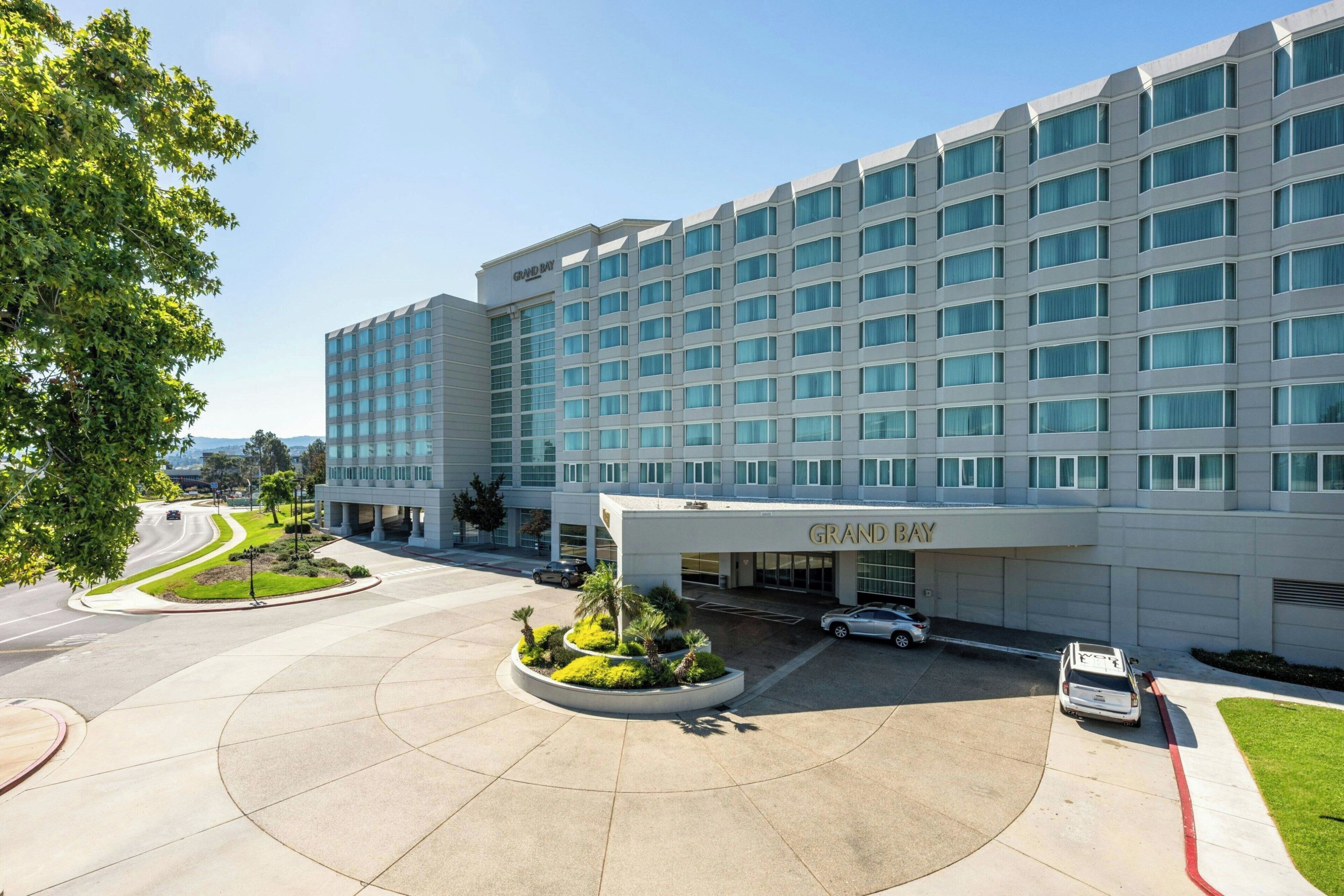 A hotel with a modern facade, a central courtyard with landscaping, and a clear sky.