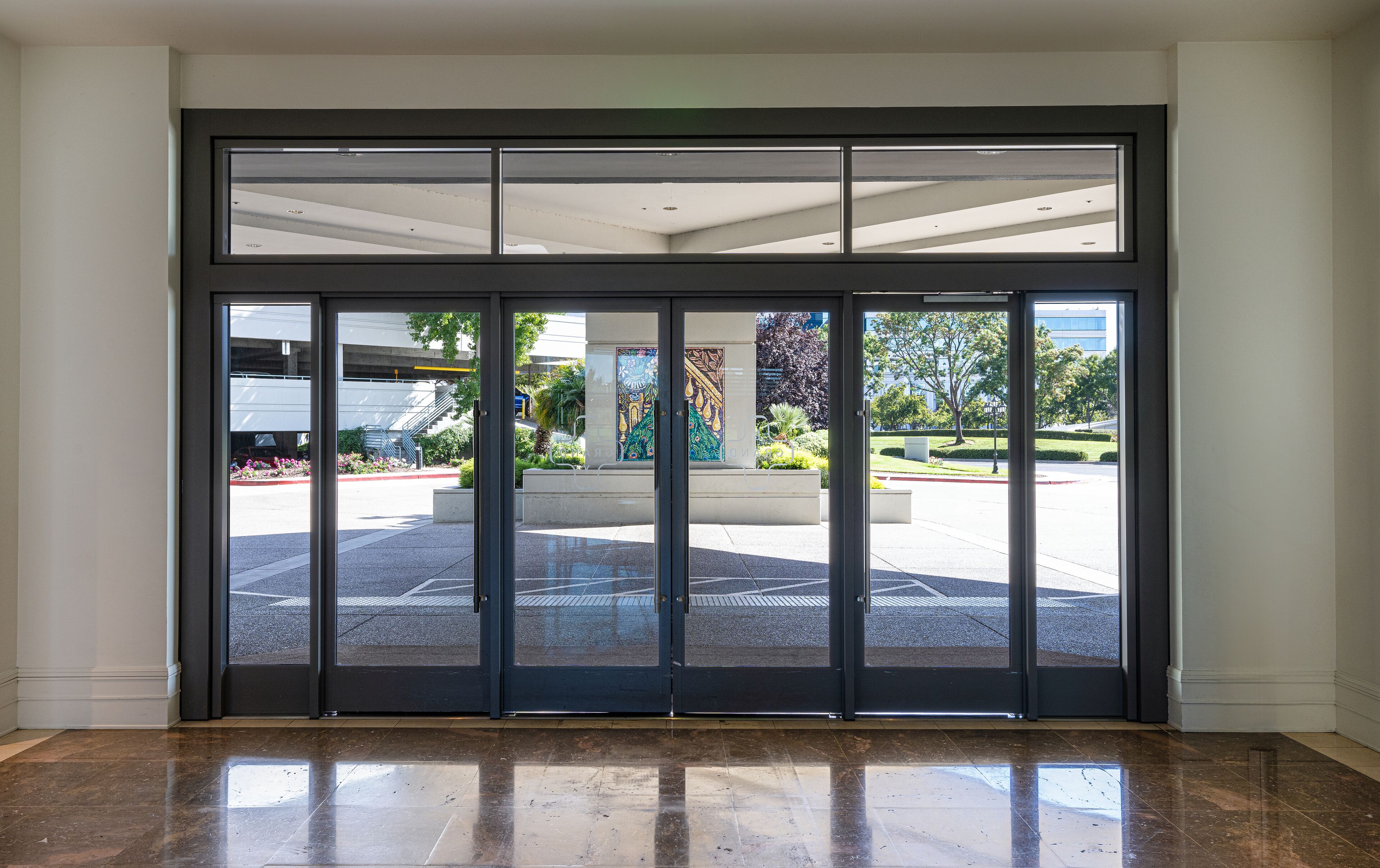A set of double doors leading to an outdoor area with a parking lot and a building in the background.