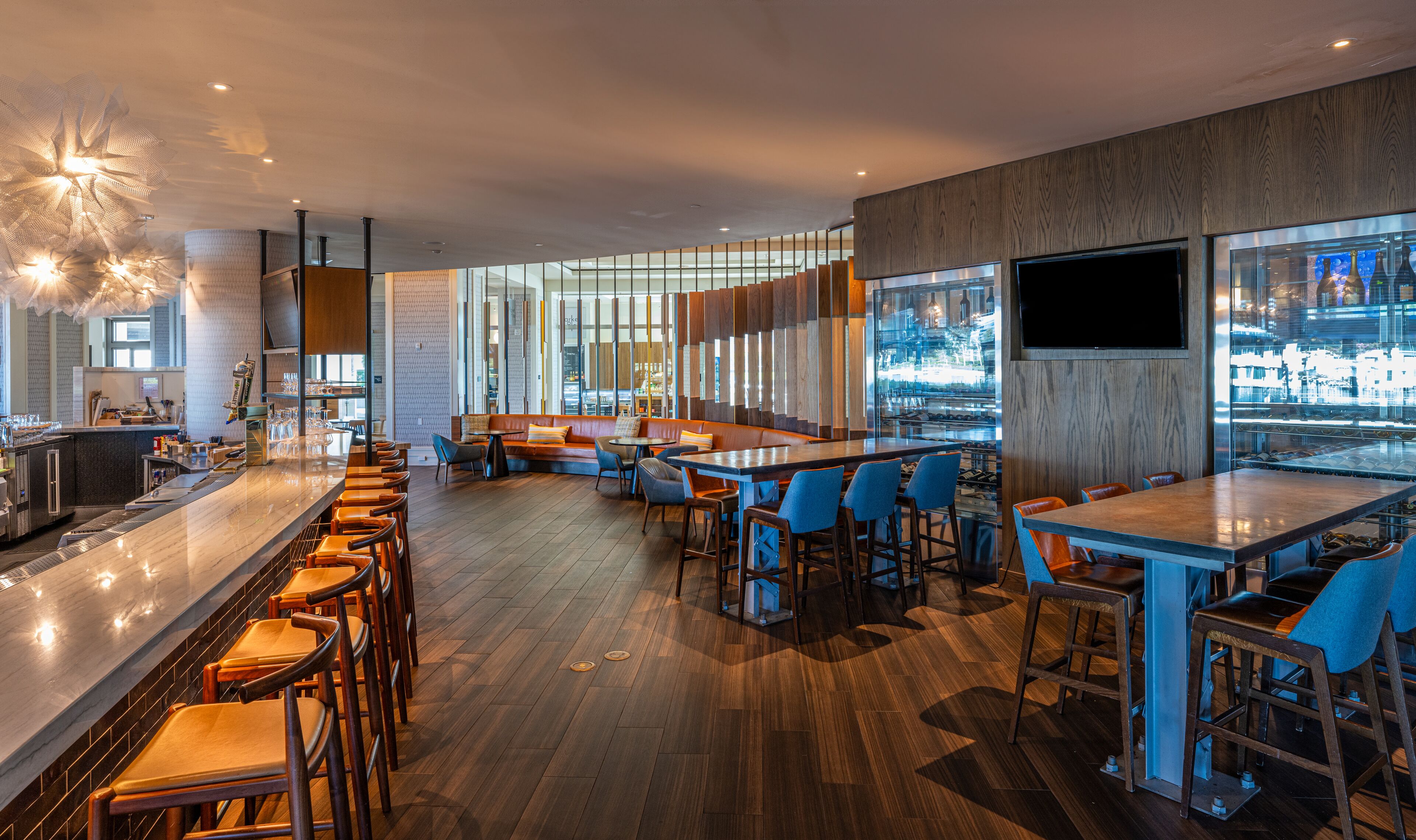 A modern bar area with wooden flooring, bar stools, and a seating area with tables and chairs.