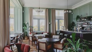 A dining area with wooden tables and chairs, a bar with shelves of bottles, and large windows with curtains. - The Queens Hotel (Portsmouth)