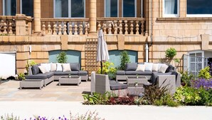 A courtyard with outdoor seating, including a sofa and chairs, surrounded by plants and flowers. - The Queens Hotel (Portsmouth)