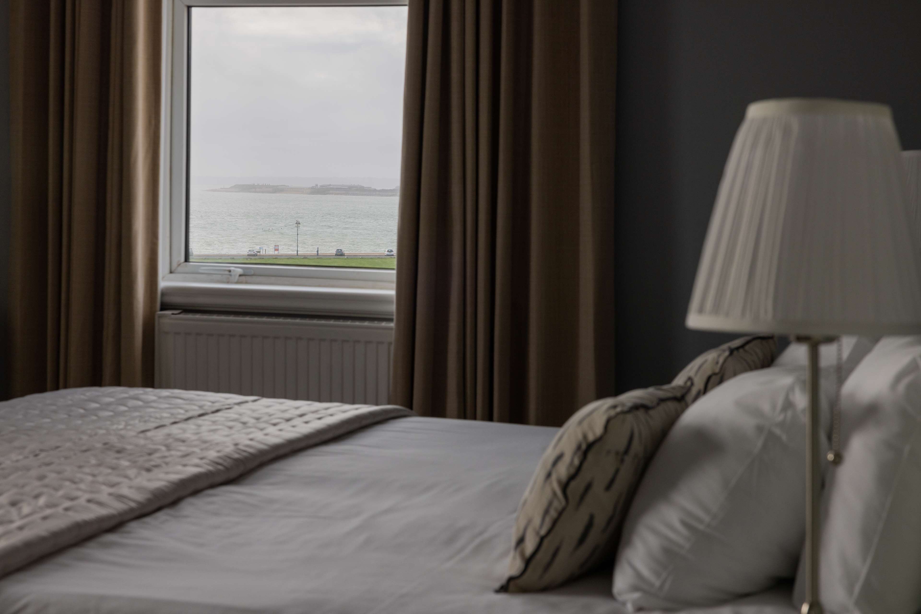 A bedroom with a bed, a window with curtains, and a lamp.