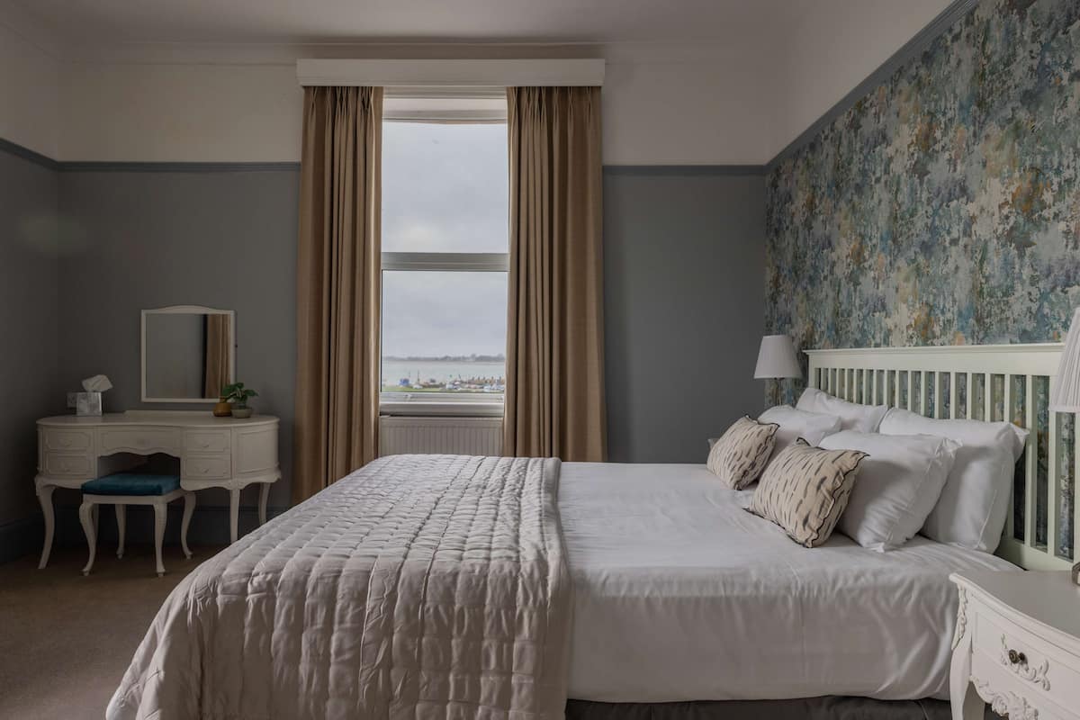 A bedroom with a large bed, a dresser, a mirror, and a view of the city through the window.