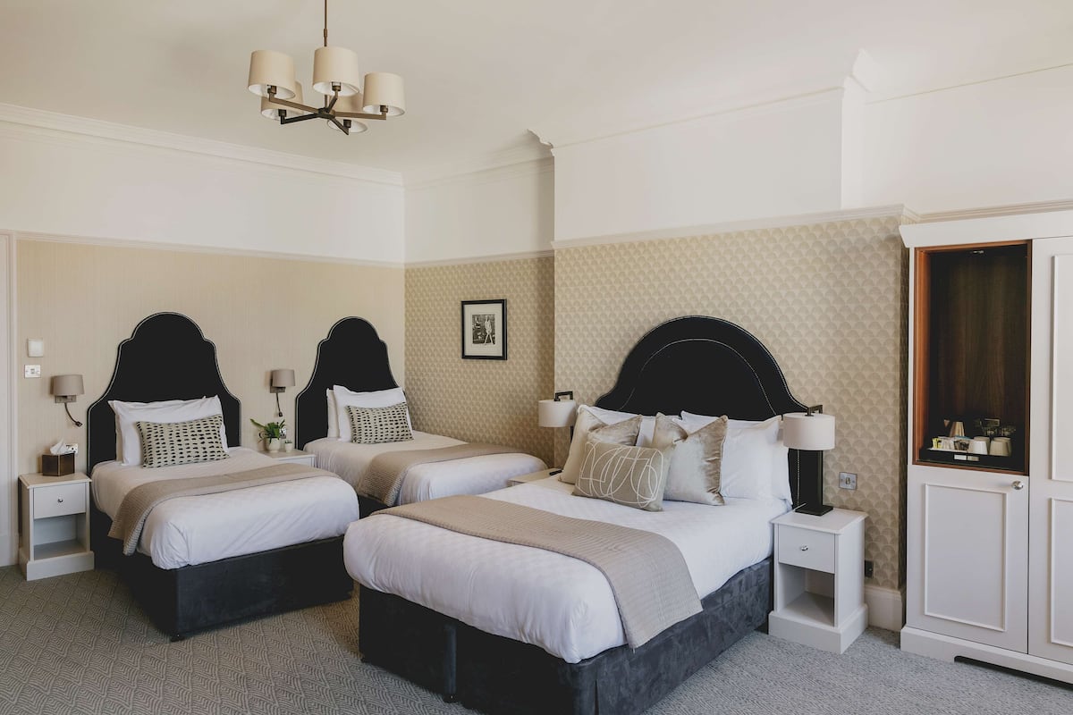 A hotel room with three beds, a wardrobe, and a chandelier.