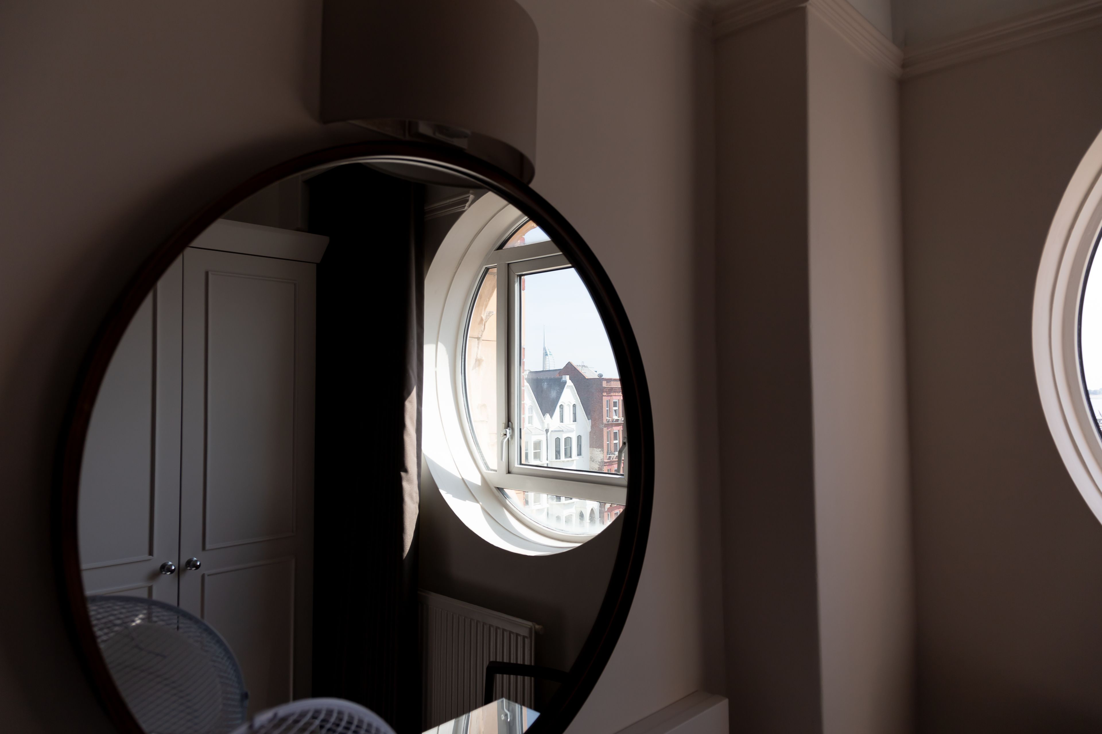 Una habitación con un espejo redondo que refleja una ventana, un radiador y una puerta.