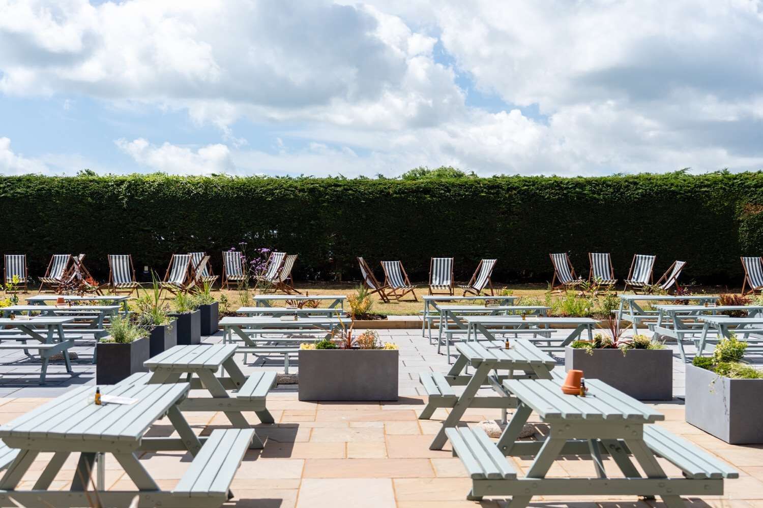 An outdoor patio area with multiple picnic tables and striped lounge chairs arranged in rows.