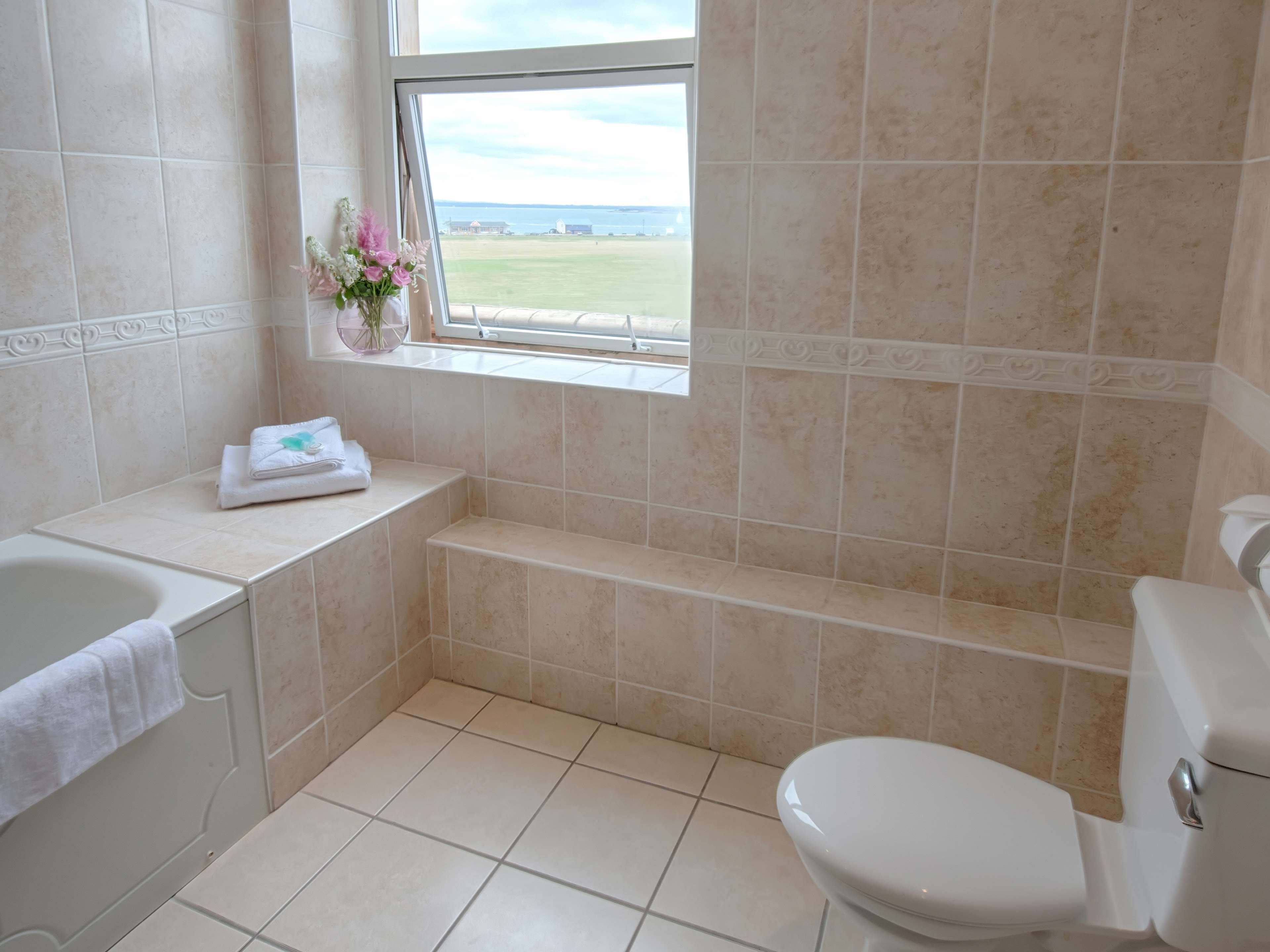 A bathroom with a bathtub, toilet, and a window with a view of the sea.