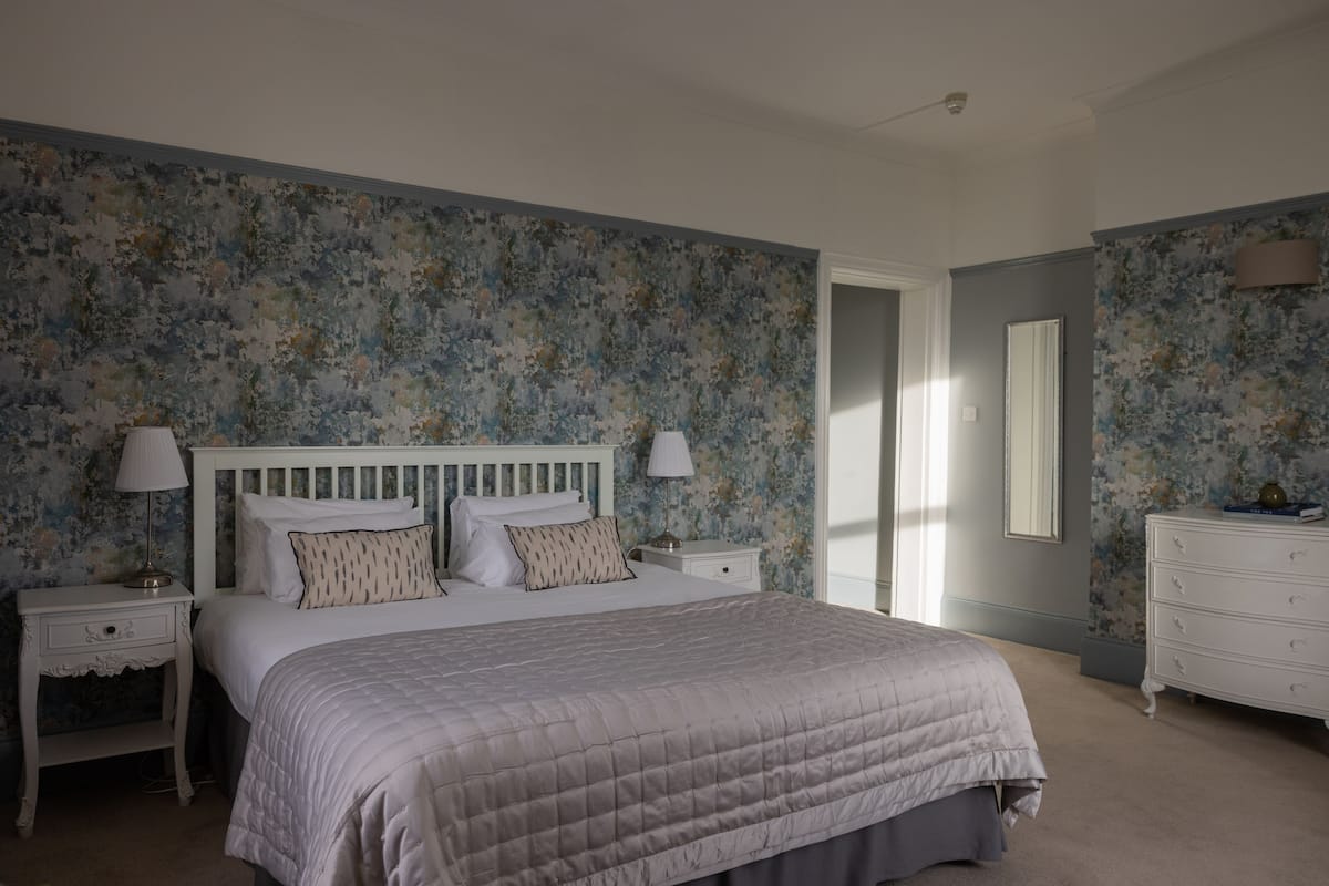 A bedroom with a bed, nightstands, a dresser, and floral wallpaper.