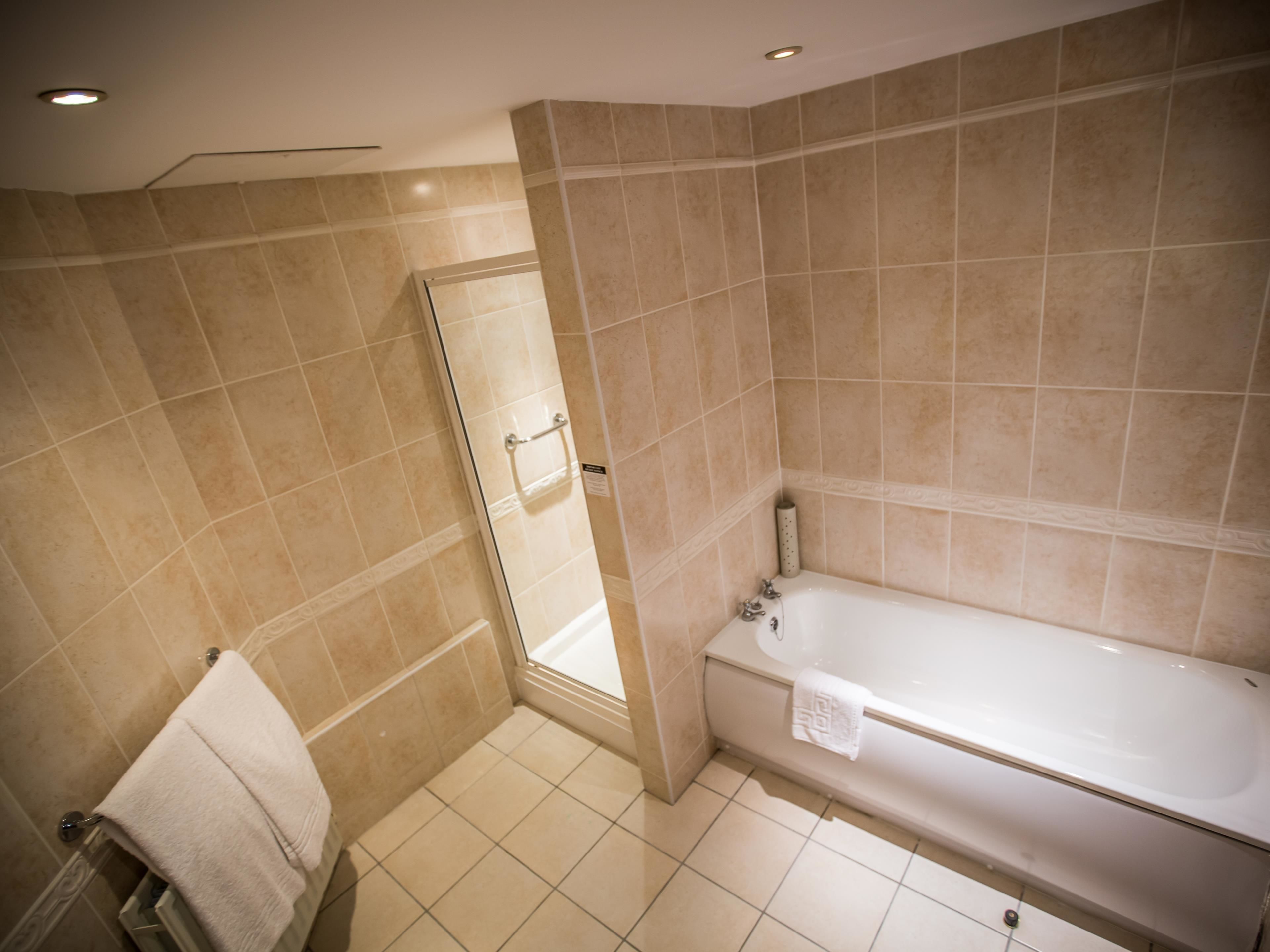 Une salle de bain avec des carreaux de couleur beige, une douche en verre, une baignoire blanche et un porte-serviettes.