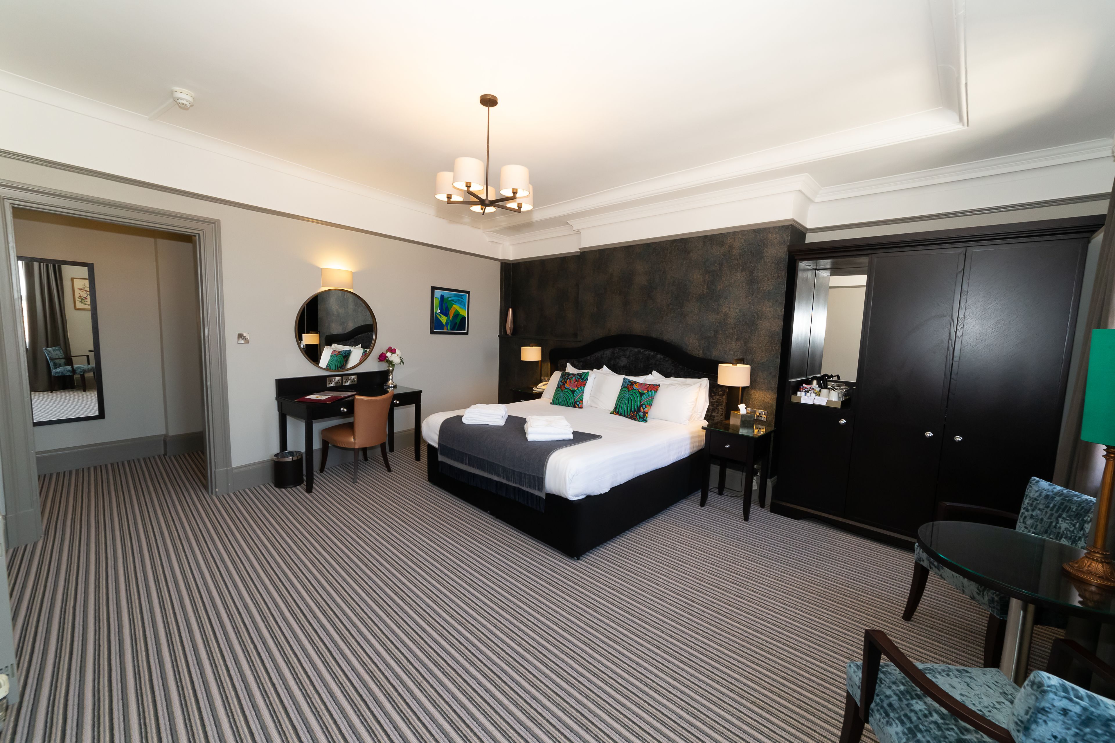 Habitació d'hotel amb un llit gran, una taula de treball, una cadira, un armari i un mirall.