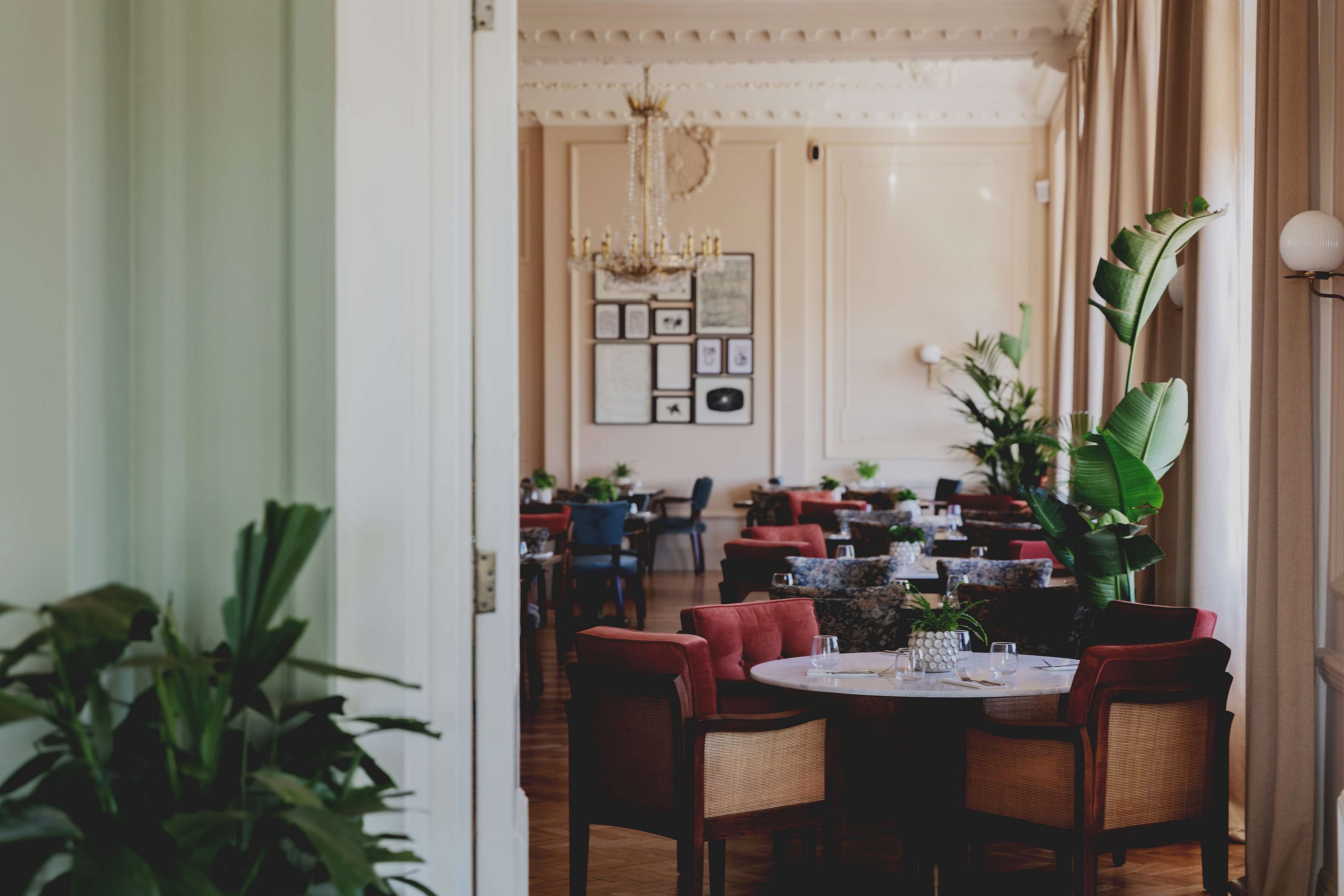 A restaurant with round tables, red upholstered chairs, and a chandelier.