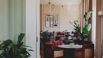 A restaurant with round tables, red upholstered chairs, and a chandelier.
