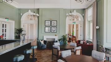 Un salon spacieux doté d’un parquet en bois à motifs chevrons, d’une cheminée centrale et d’un coin bar avec des tabourets.