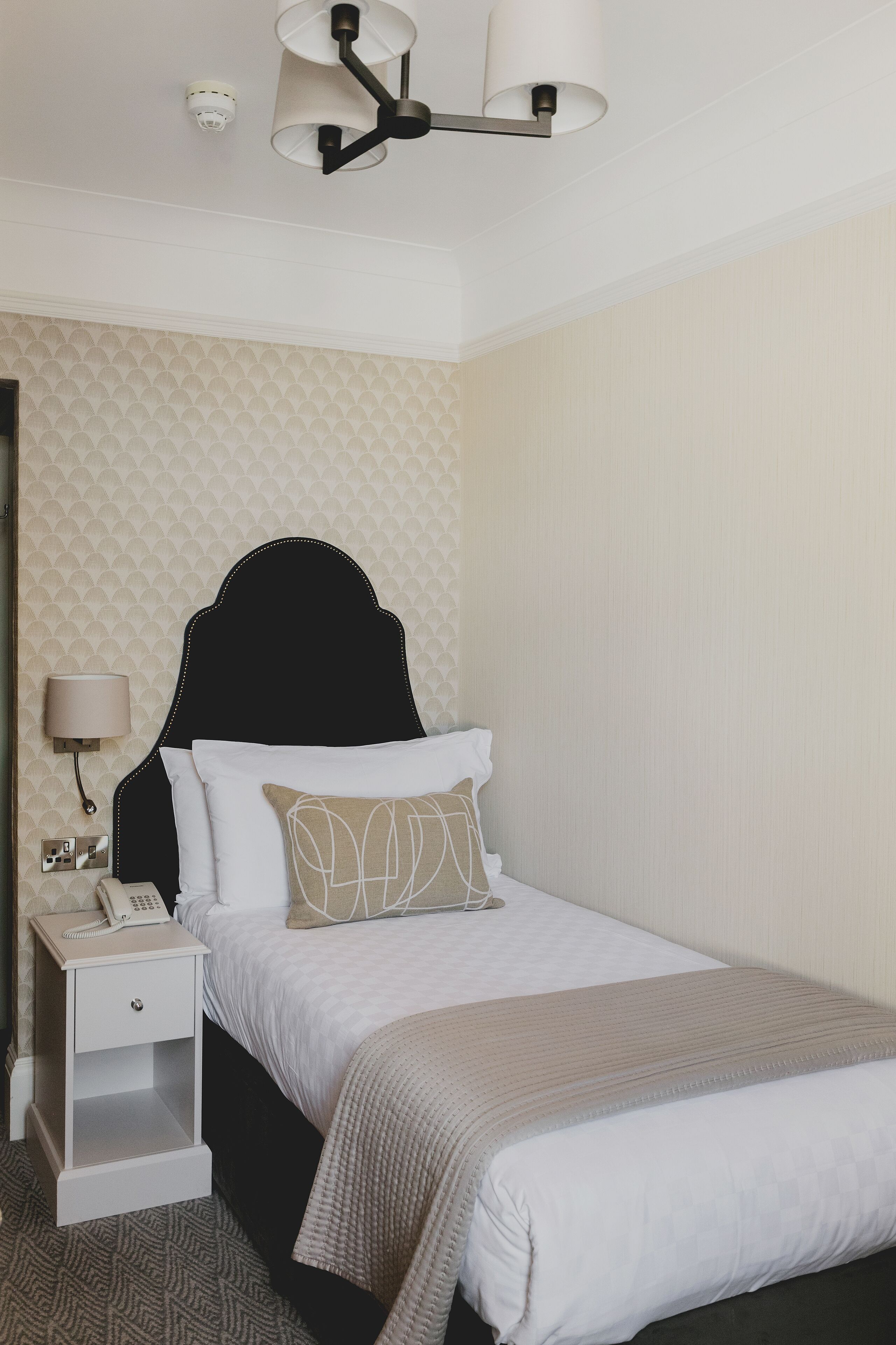 Een keurig opgemaakt bed met een zwart hoofdeinde, een bedlampje en een telefoon op een nachtkastje.