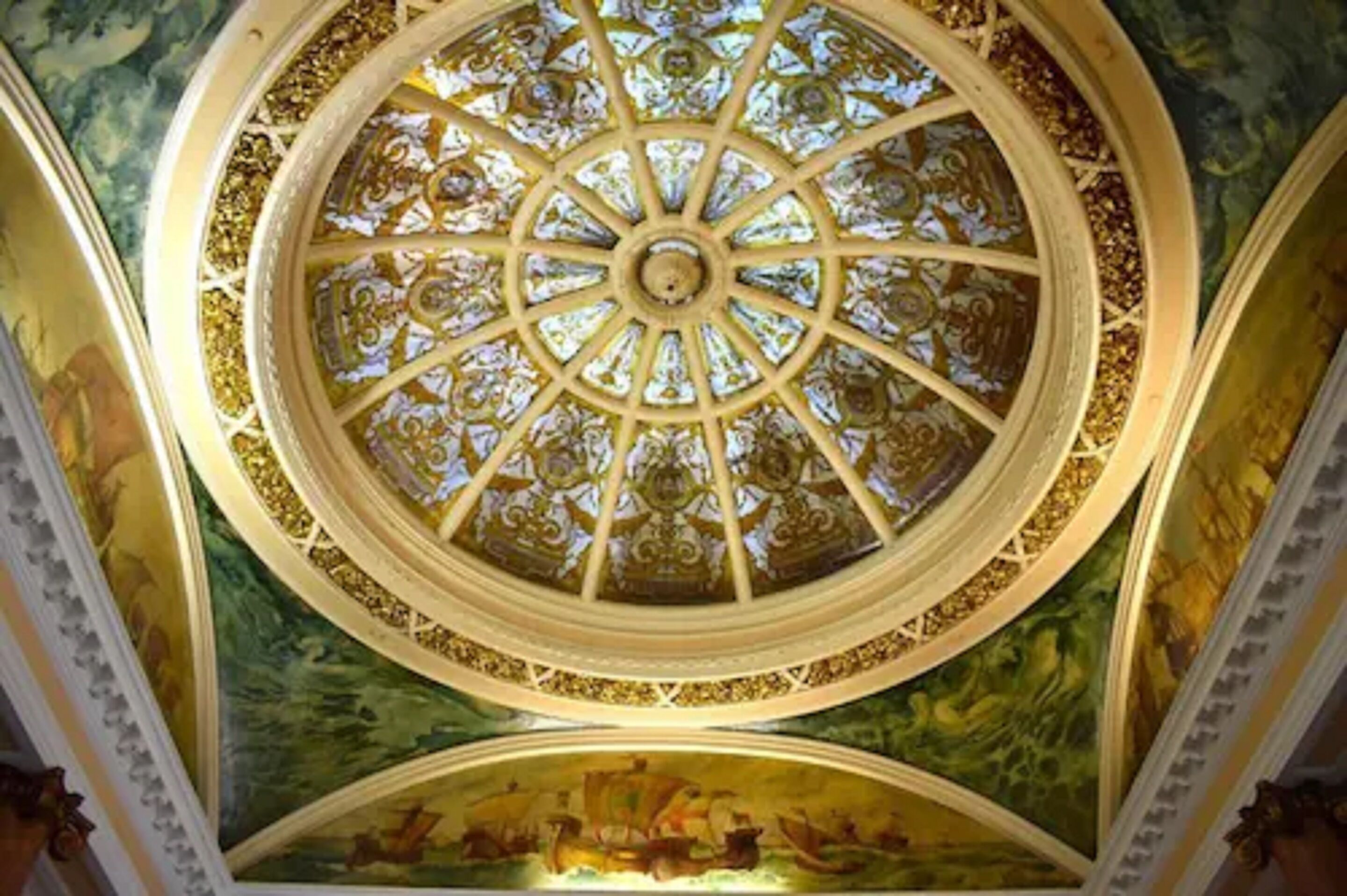 A detailed ceiling with a central stained glass window and surrounding frescoes.