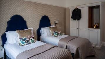 Une chambre d’hôtel avec deux lits, chacun doté d’une tête de lit, d’une table de chevet et d’une lampe. On y trouve également une armoire avec un manteau suspendu.