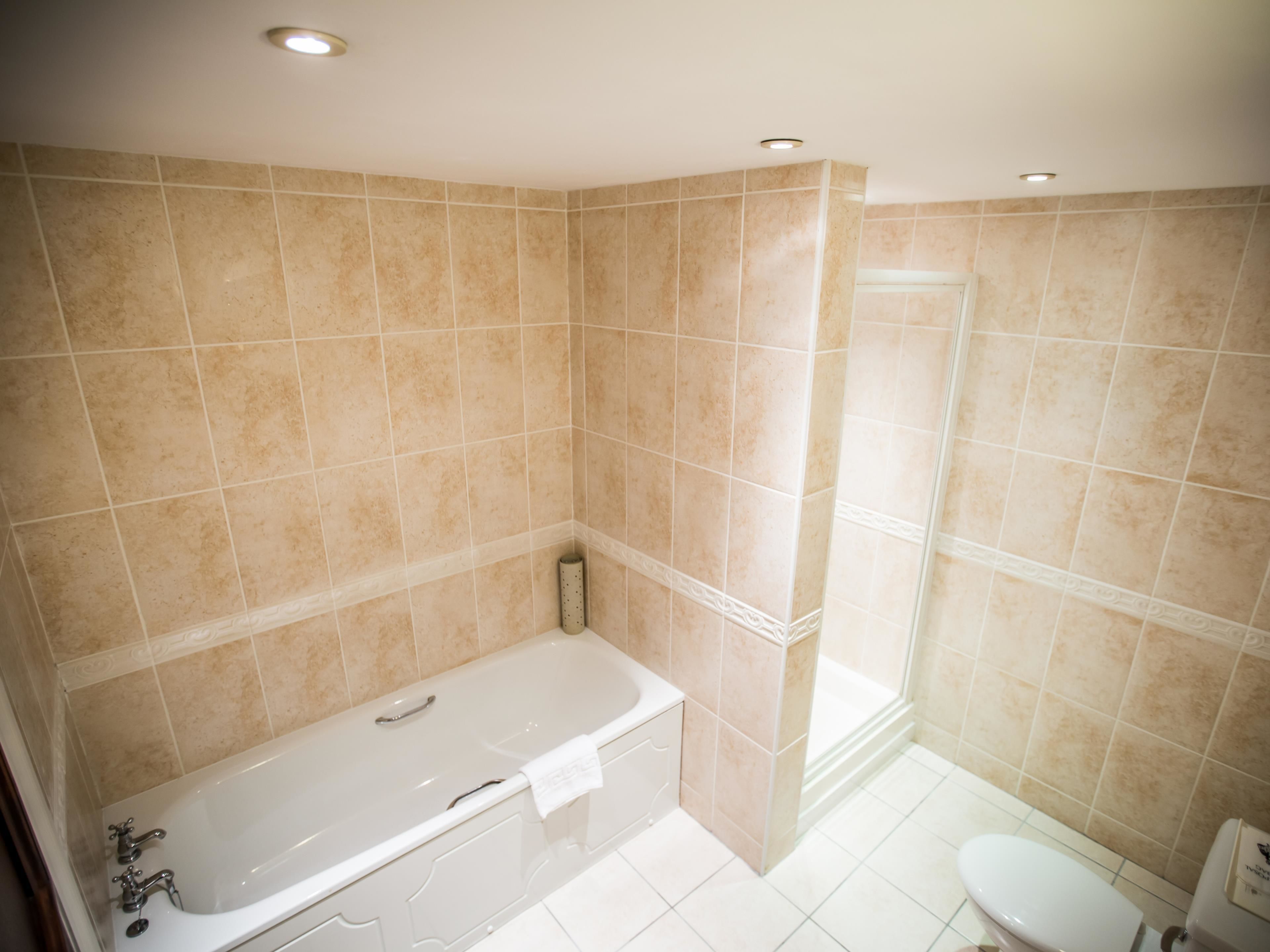 Ein Badezimmer mit beigen Fliesen, einer Badewanne, einer Toilette und einer Duschkabine.