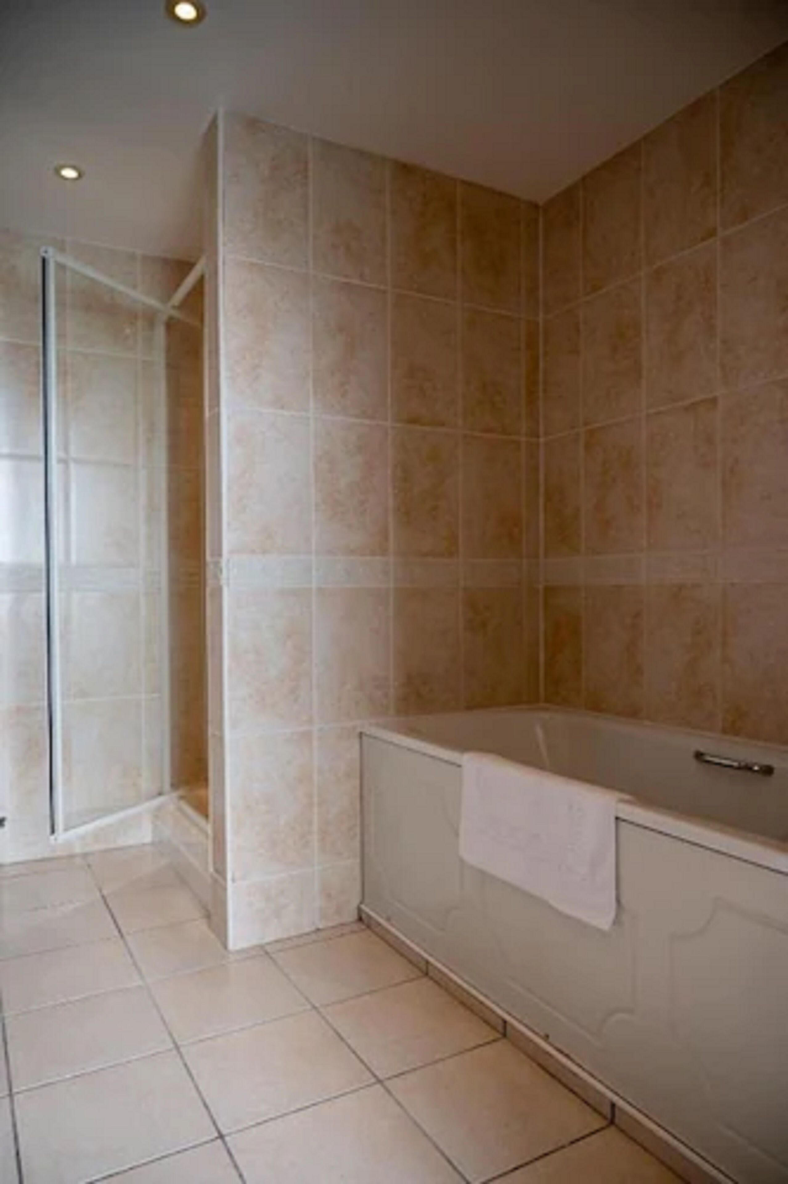Un baño con baldosas color crema, cabina de ducha de vidrio y bañera con una toalla.