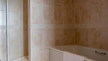 Un baño con baldosas color crema, cabina de ducha de vidrio y bañera con una toalla.