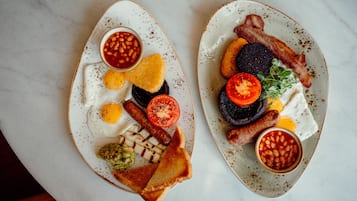Two plates of breakfast with eggs, sausages, bacon, toast, and beans.