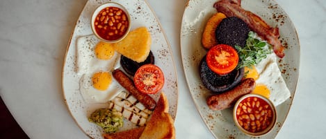 Two plates of breakfast with eggs, sausages, bacon, toast, and beans.