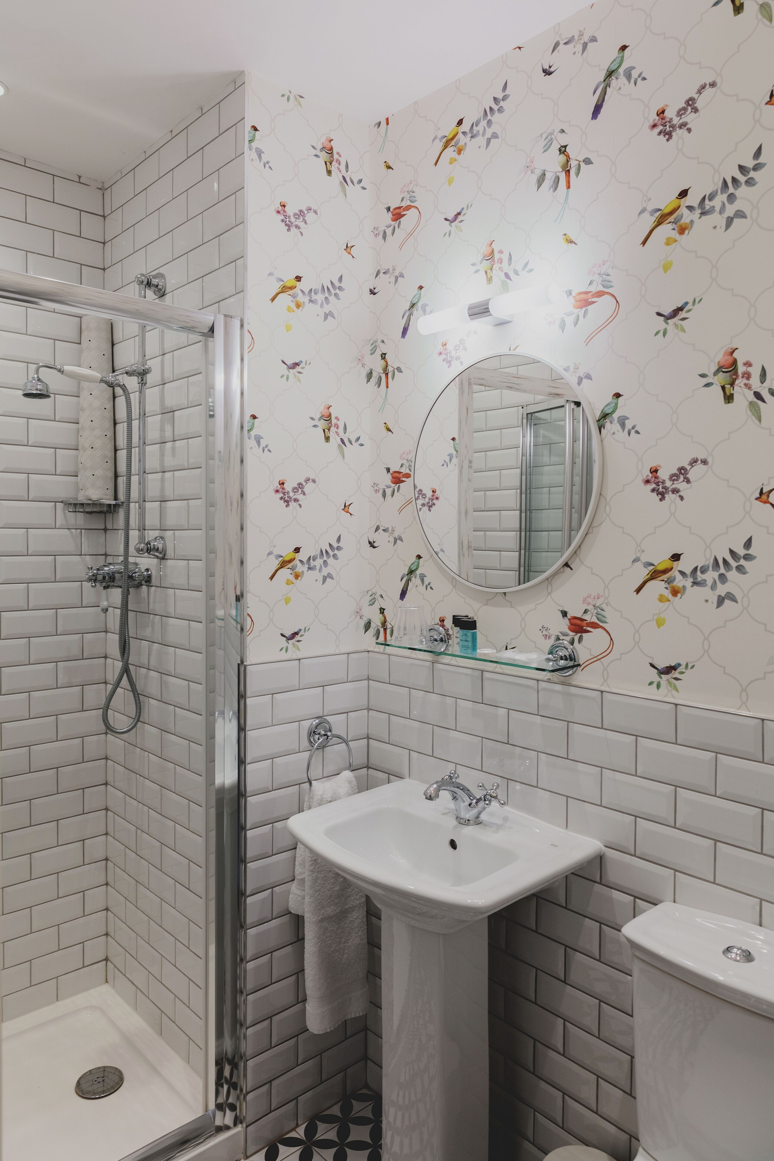A bathroom with white tiled walls, a shower, a sink, and a toilet.