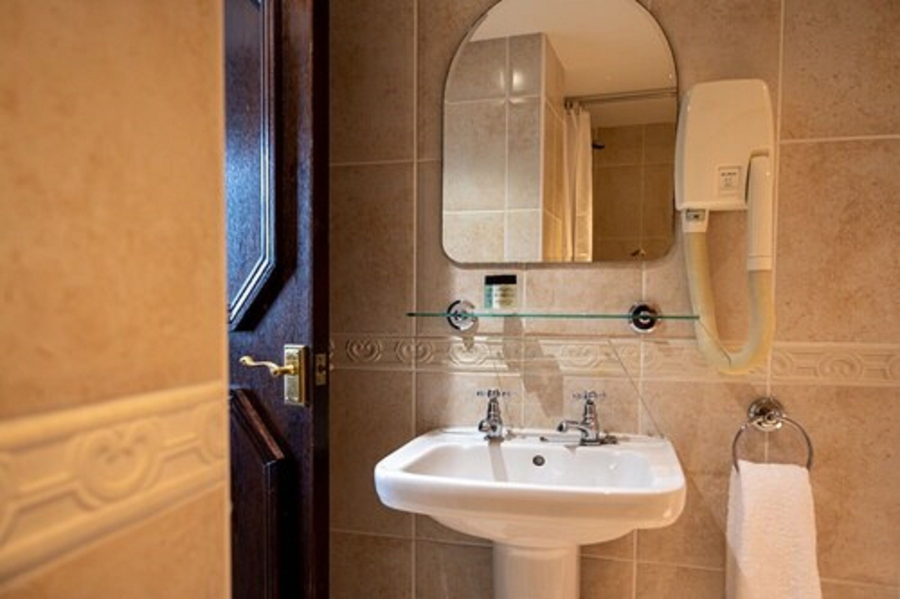 A bathroom with a white sink, a glass shelf, a mirror, and a towel rack.