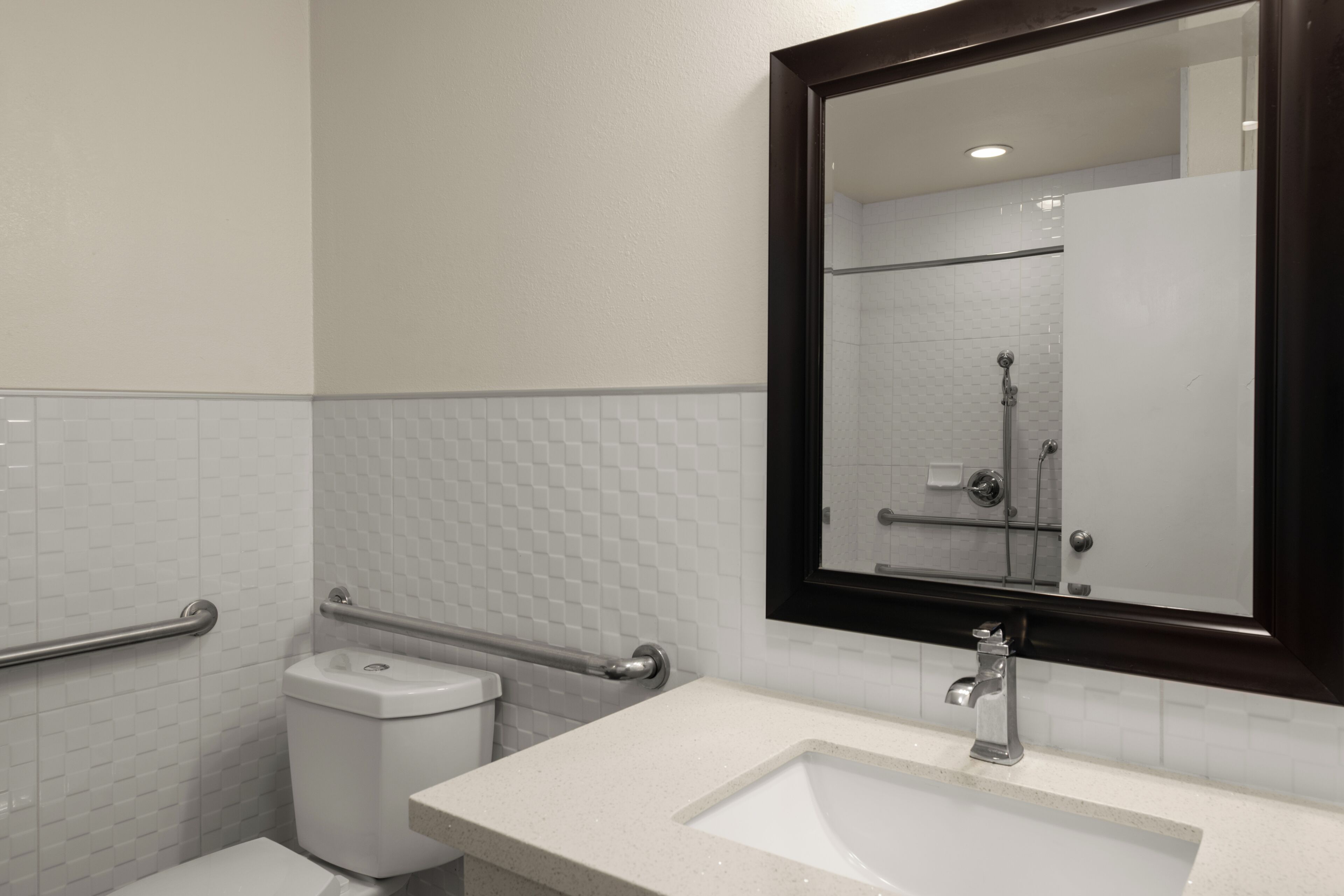 A bathroom with a white tiled wall, a white sink, a mirror, and a shower area.