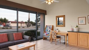 A modern room with a sofa, a coffee table, a desk, and a large window offering a view of the street. - Sand Dollar Inn (Seaside)