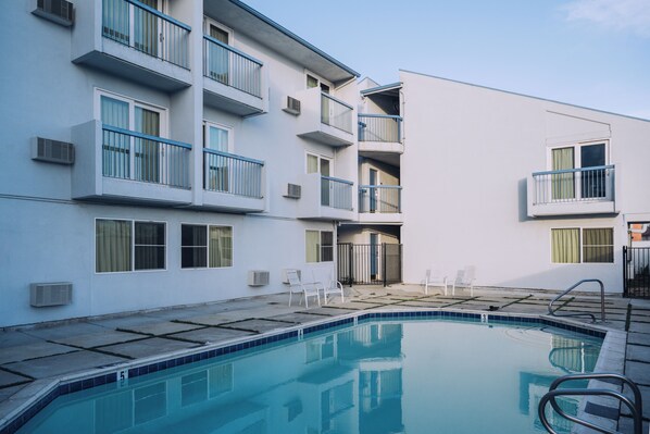 A swimming pool with a clear blue water, surrounded by a white building with balconies and windows. - Sand Dollar Inn (Seaside)