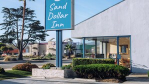 A hotel sign, 'Sand Dollar Inn,' with a modern building facade, a clear sky, and surrounding landscaping. - Sand Dollar Inn (Seaside)