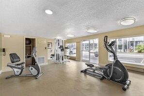 Een sportschool met cardio-apparatuur, krachttrainingsmaterialen en grote ramen met uitzicht op de straat.