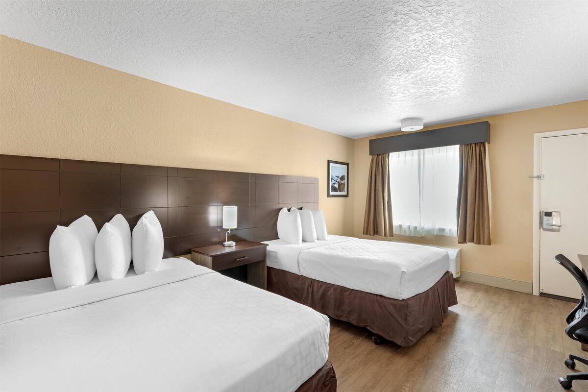 A hotel room with two beds, a desk, a chair, and a window with curtains.