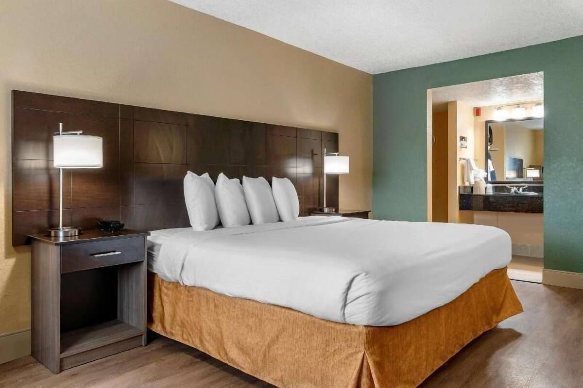 A hotel room with a large bed, two bedside tables, a desk, and a bathroom visible through an open door.